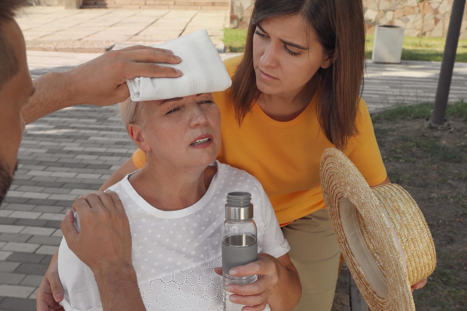 Ältere Frau mit Kreislaufproblem wird von einer Frau und einem Mann betreut.