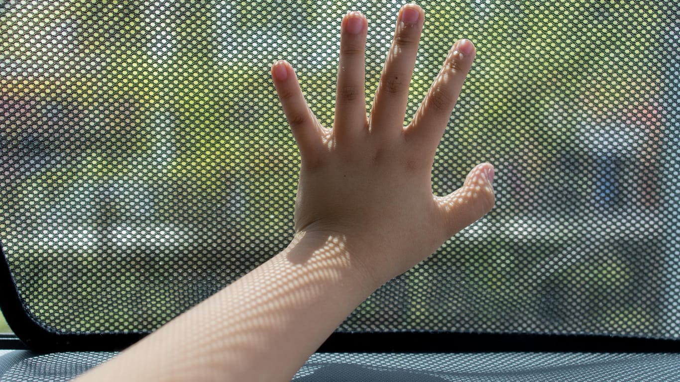 Kinderhand auf Sonnenblende eines Autofensters