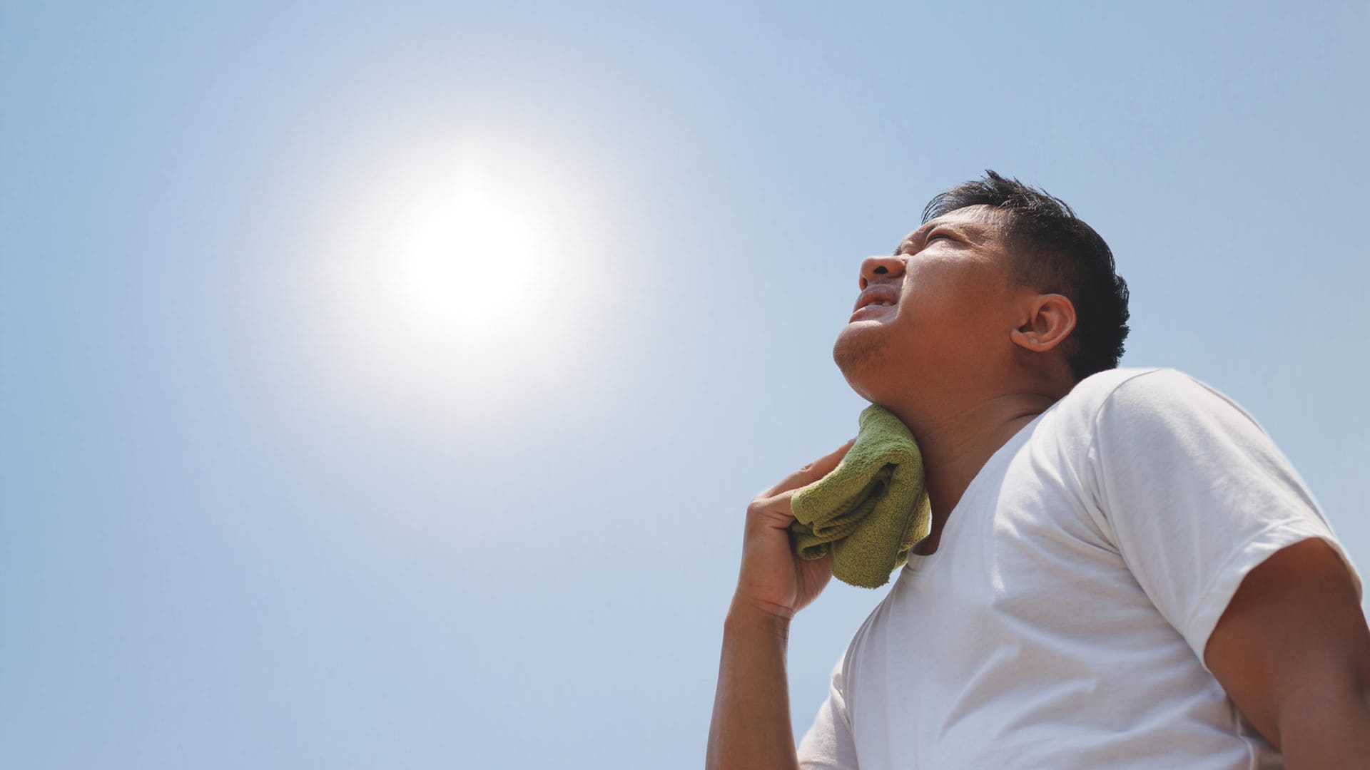 Mann mit Handtuch schaut in die pralle Sonne.