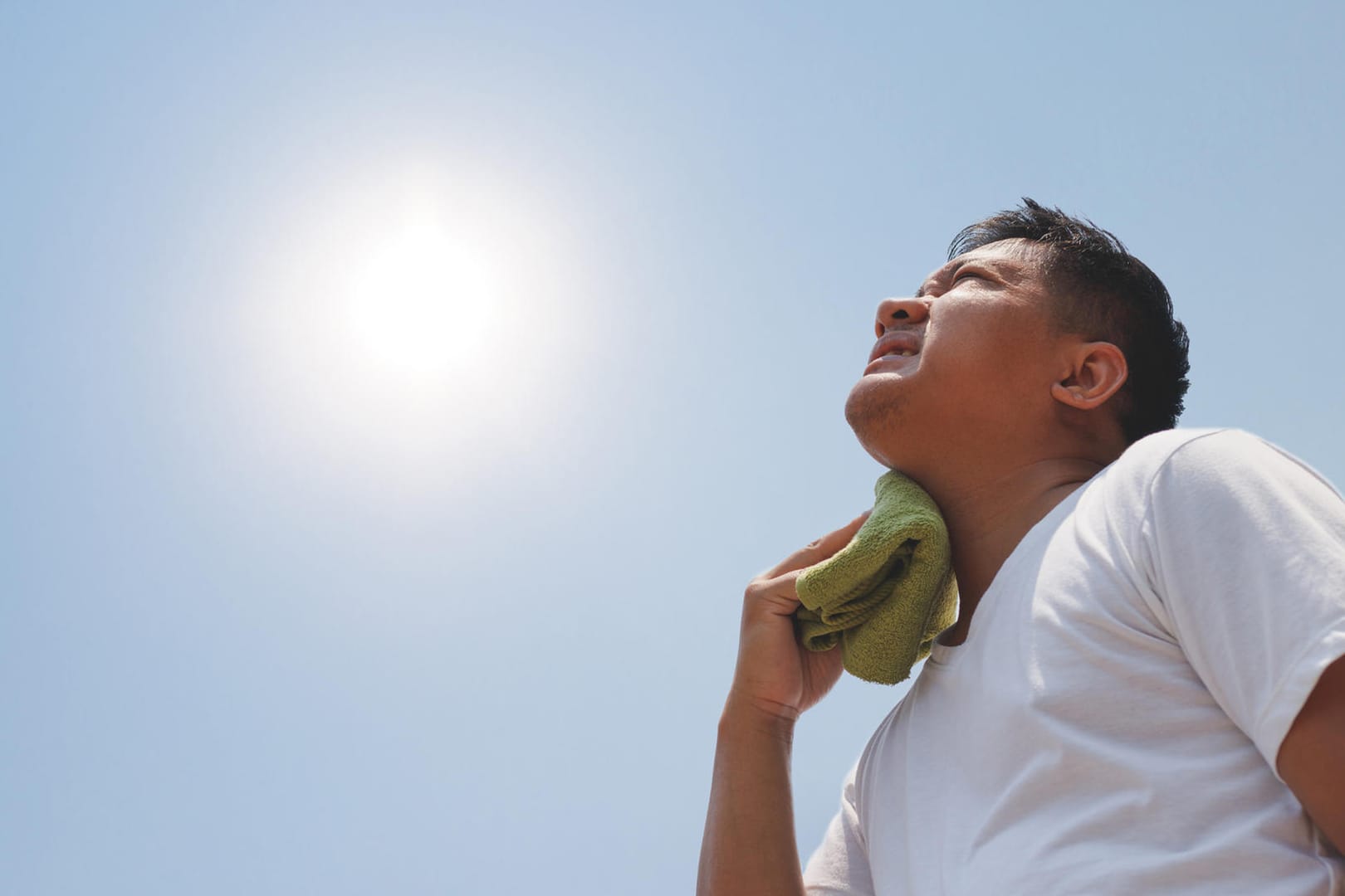 Mann mit Handtuch schaut in die pralle Sonne.