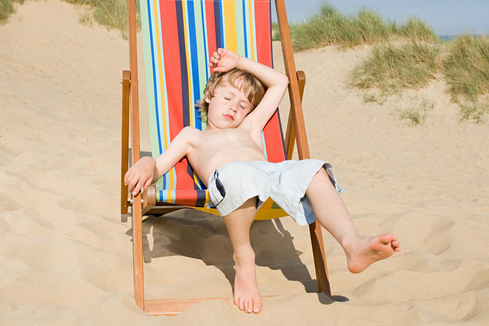 Junge sitzt erschöpft im Stuhl am Strand.