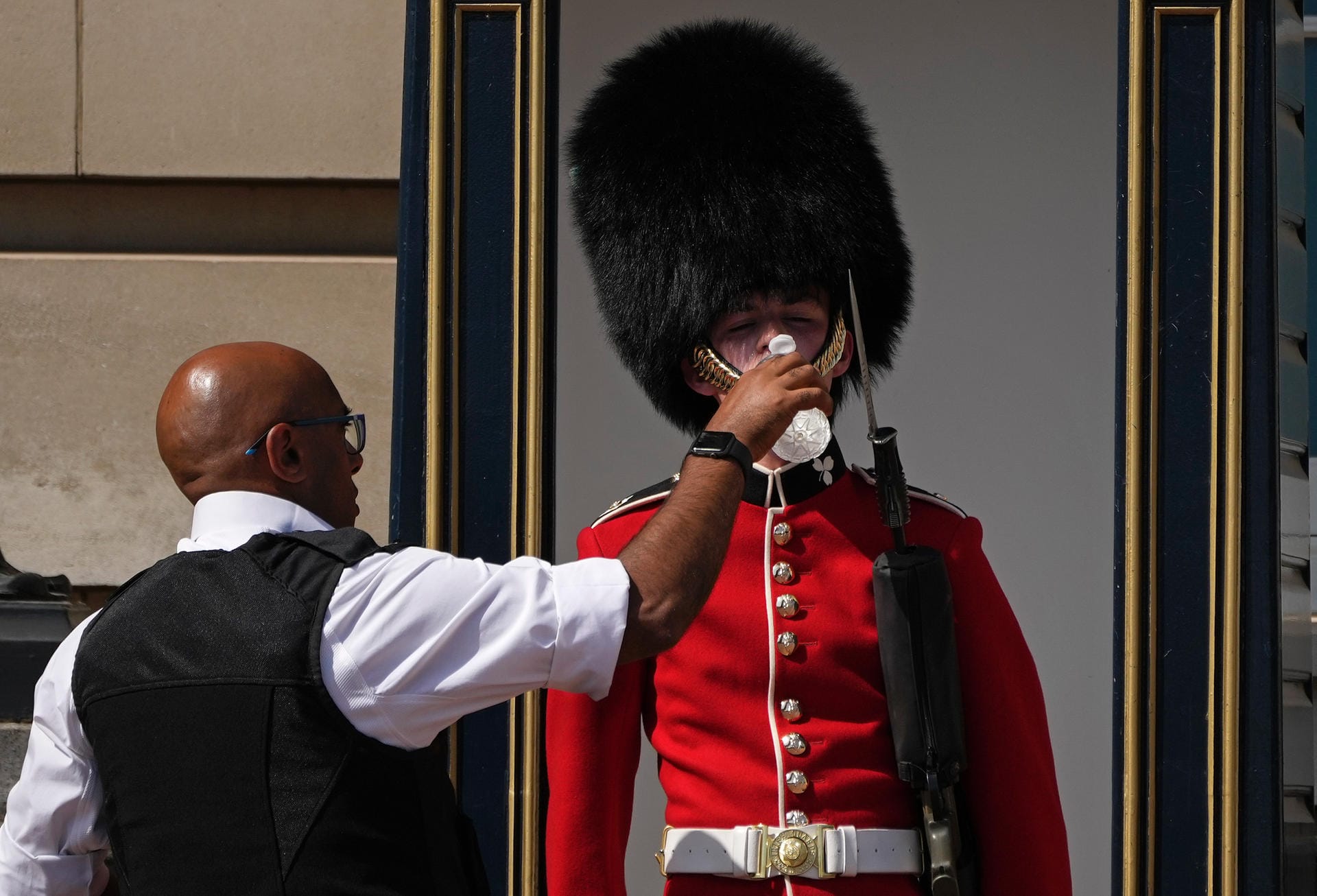 London, Großbritannien: Ein Polizeibeamter gibt einem britischen Soldaten, der eine traditionelle Bärenfellmütze trägt, während seines Wachdienstes vor dem Buckingham Palast Wasser.