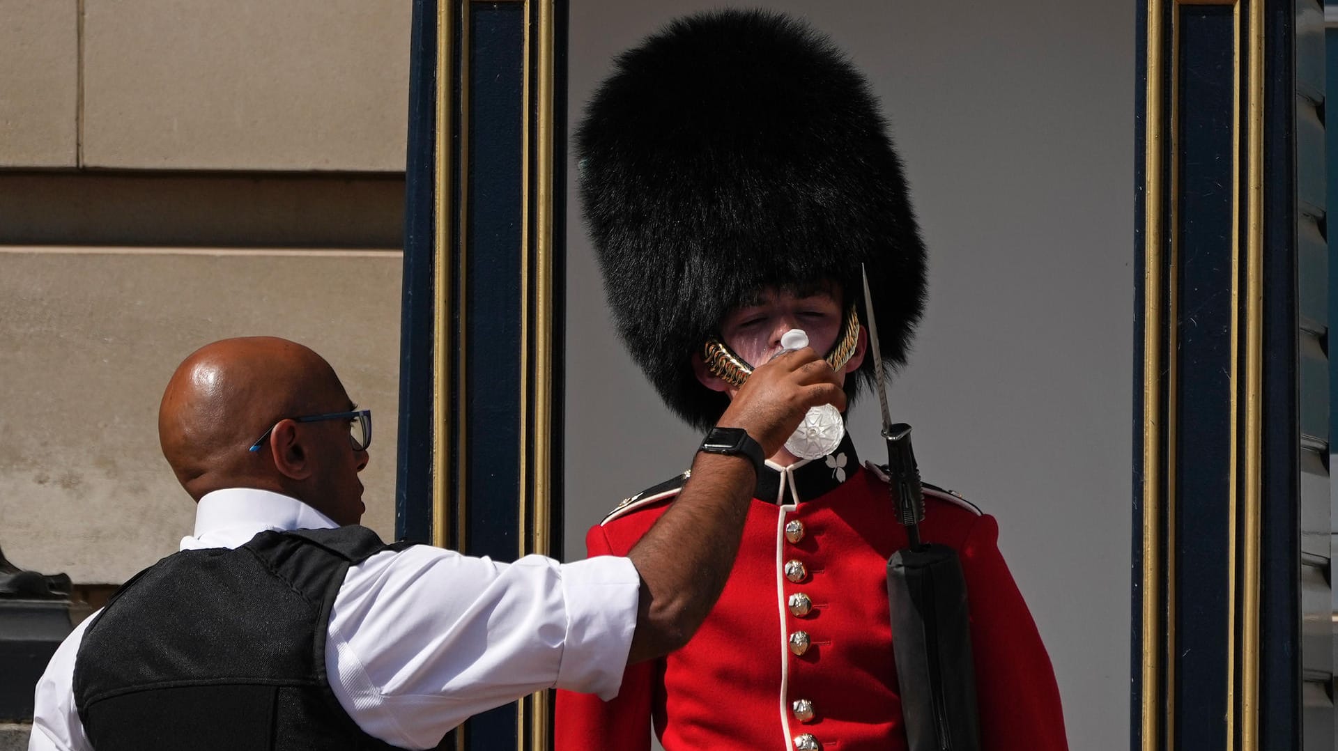 London, Großbritannien: Ein Polizeibeamter gibt einem britischen Soldaten, der eine traditionelle Bärenfellmütze trägt, während seines Wachdienstes vor dem Buckingham Palast Wasser.