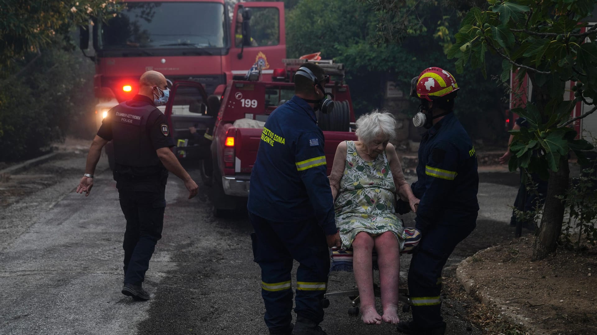 Feuerwehrleute bringen eine ältere Frau aus ihrem Haus: Meteorologen befürchten weitere Brände.