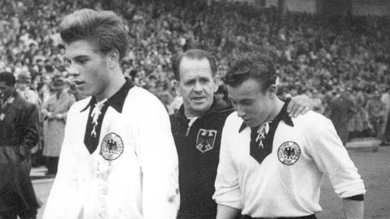 Niedergeschlagen gehen die Debütanten Klaus Stürmer (l) und Uwe Seeler (r) mit Bundestrainer Sepp Herberger zur Halbzeit in die Kabine.