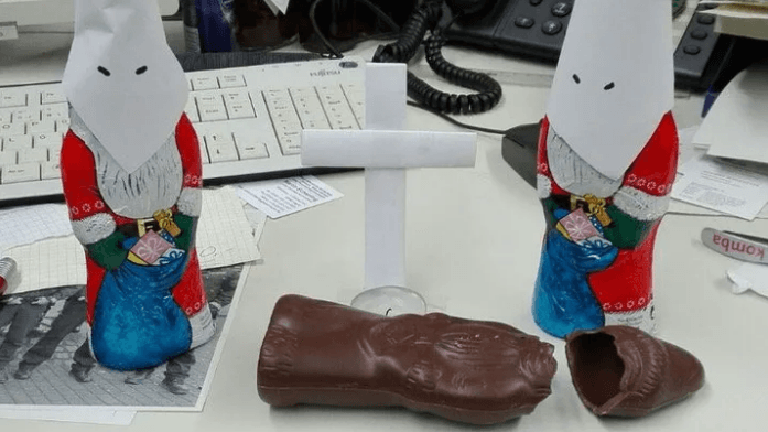 Das Foto zeigt zwei Schoko-Nikoläuse mit weißen Kapuzen des Ku-Klux-Klans. Davor liegt ein enthüllter, brauner Schoko-Nikolaus. Das Foto zeigt zwei Schoko-Nikoläuse mit weißen Kapuzen des Ku-Klux-Klans. Davor liegt ein enthüllter, brauner Schoko-Nikolaus.