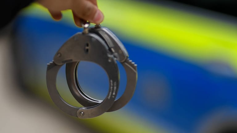 Ein Polizist mit Handschellen (Archivbild): In Berlin ist ein Mann direkt nach seiner Entlassung wieder festgenommen worden.