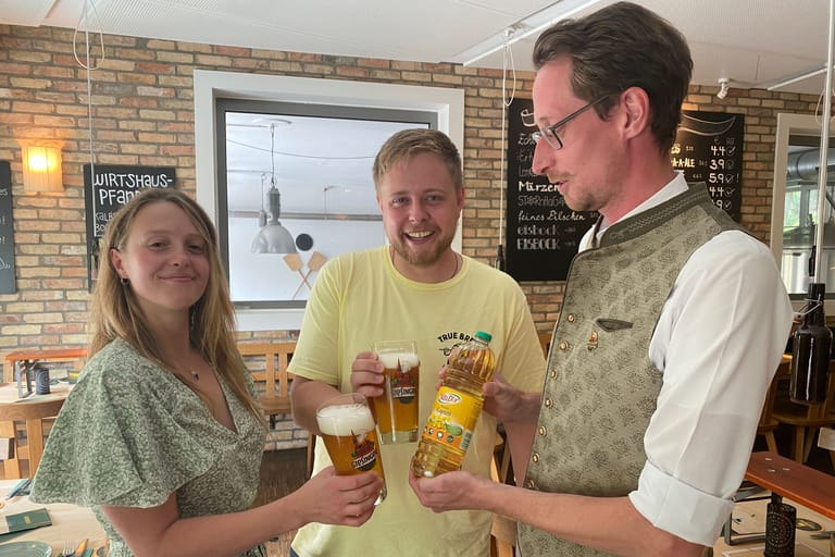 Restaurantleiter Erik Hoffmann von der Giesinger Brauerei (rechts) tauscht mit zwei Gästen Bier gegen Öl. Die Brauerei bietet den Tausch jetzt an, weil Speiseöl knapp wurde.