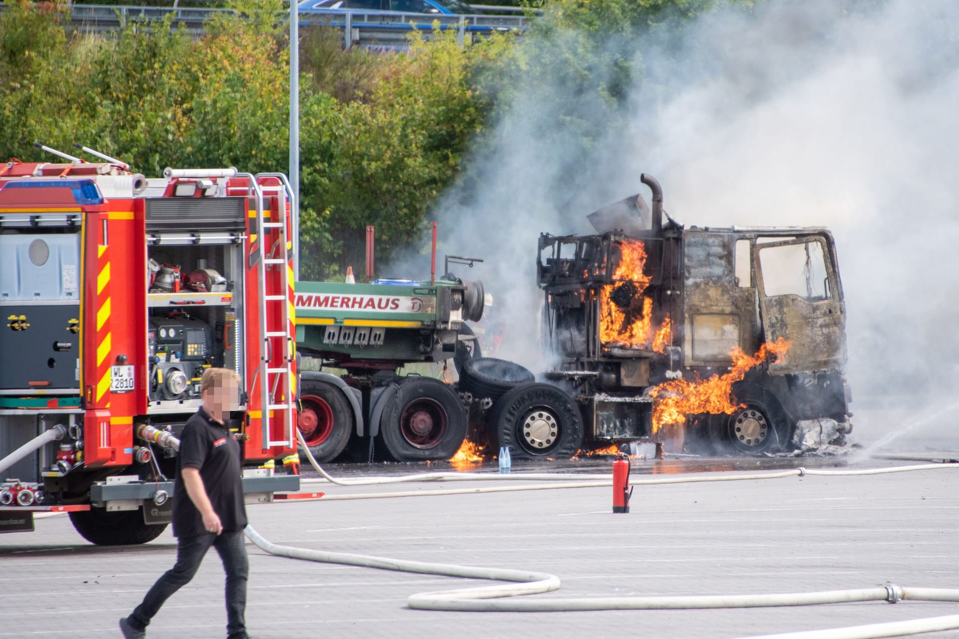 Der Lkw steht in Flammen, daneben steht ein Einsatzfahrzeug der Feuerwehr.