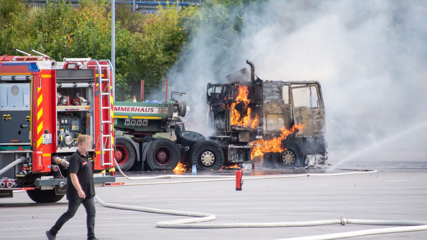 Der Lkw steht in Flammen, daneben steht ein Einsatzfahrzeug der Feuerwehr.
