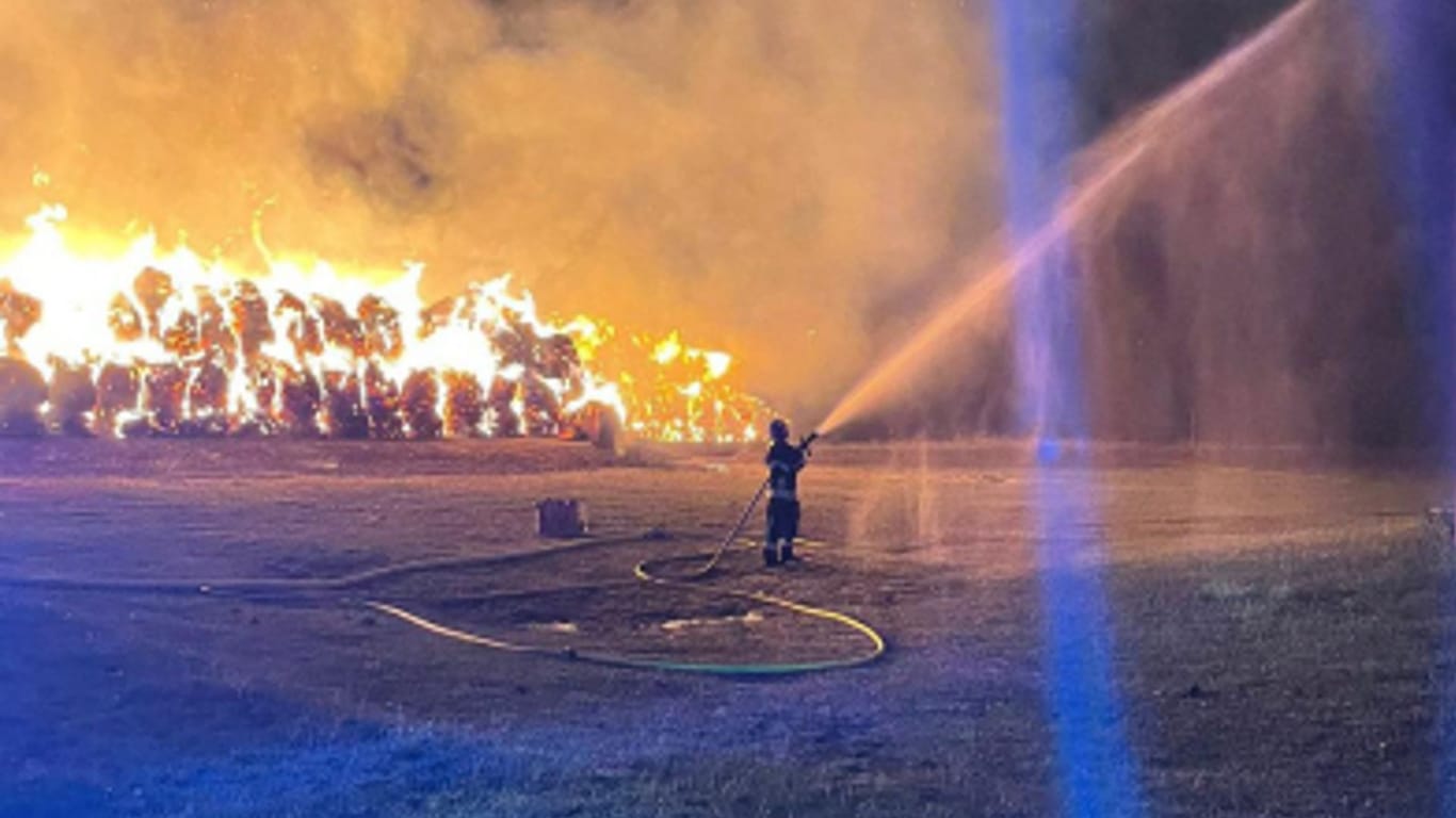 Ein Feuerwehrmann löscht die in Flammen stehenden Heuballen: Nur wenige Meter weiter befinden sich empfindliche Gastanks.
