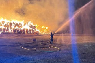 Ein Feuerwehrmann löscht die in Flammen stehenden Heuballen: Nur wenige Meter weiter befinden sich empfindliche Gastanks.