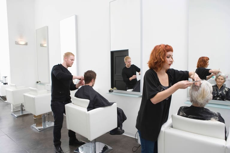 Zwei Mitarbeitende eines Friseursalons machen einem Mann und einer Frau die Haare (Symbolbild).