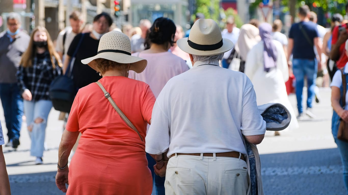 Ein älteres Ehepaar ist mit Strohhüten in einer Einkaufsmeile unterwegs: Die Dtadt Köln rät, bei Hitze Kopfbedeckungen zu tragen.