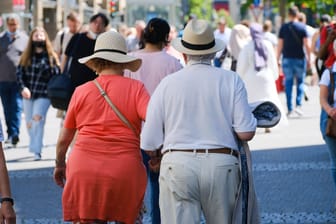 Ein älteres Ehepaar ist mit Strohhüten in einer Einkaufsmeile unterwegs: Die Dtadt Köln rät, bei Hitze Kopfbedeckungen zu tragen.