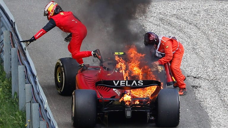 Carlos Sainz rettet sich aus dem brennenden Ferrari, ein Streckenposten löscht das Feuer.