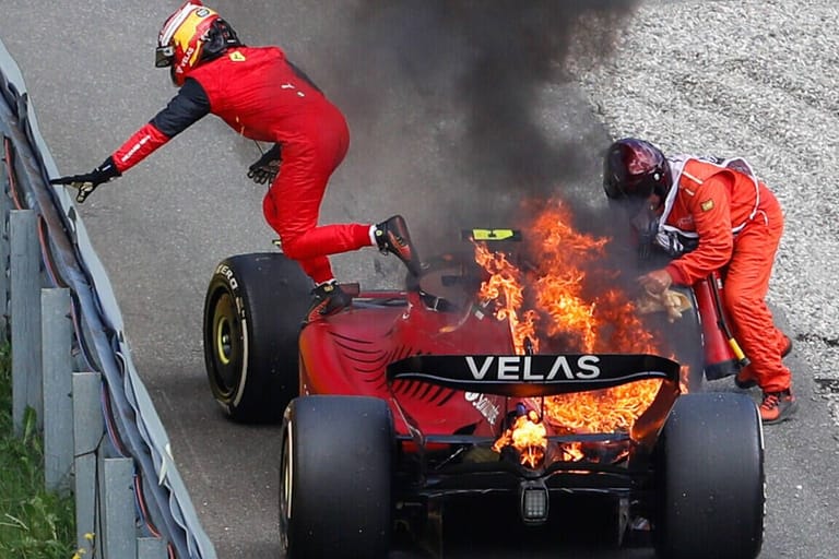 Carlos Sainz rettet sich aus dem brennenden Ferrari, ein Streckenposten löscht das Feuer.