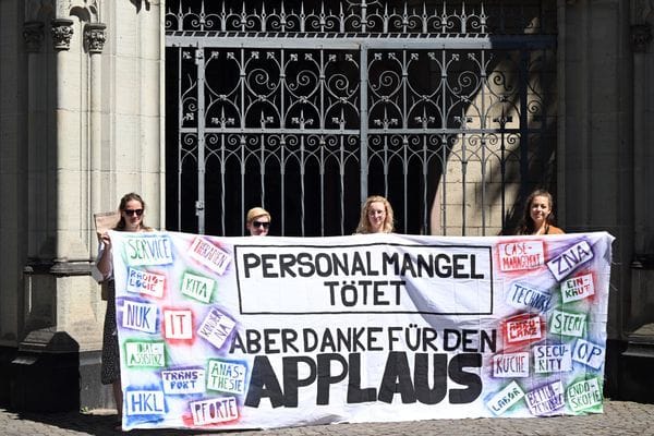 Uniklinik-Beschäftige mit Plakat: Eindrückliche Erfahrungsberichte, vorgelesen in einer Kölner Kirche, sollen aufrütteln.