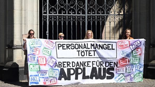 Uniklinik-Beschäftige mit Plakat: Eindrückliche Erfahrungsberichte, vorgelesen in einer Kölner Kirche, sollen aufrütteln.