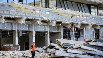 Ein Ordner mit Bauhelm und Warnweste steht an der abgerissenen Tribüne in der Mercedes-Benz Arena.