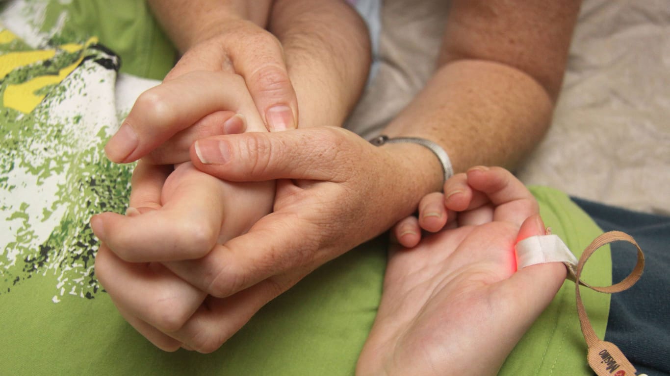 Eine Frau hält im Kinderhospiz Löwenherz die Hand ihres Kindes: Das Hospiz muss wegen Personalnot sein Angebot einschränken.