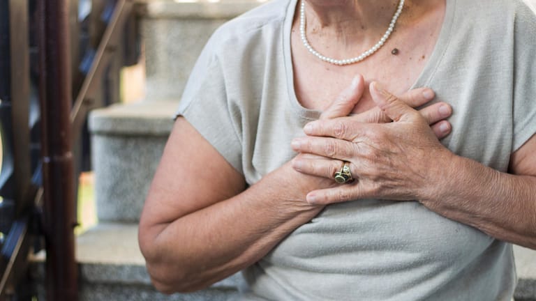 Ältere Fau greift sich ans Herz. Luftnot, Müdigkeit und schnelle Erschöpfung sind typische Warnzeichen für eine Herzschwäche und sollten frühzeitig von einem Arzt abgeklärt werden. In seltenen Fällen kann eine kardiale Amyloidose dahinterstecken.