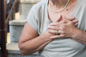 Ältere Fau greift sich ans Herz. Luftnot, Müdigkeit und schnelle Erschöpfung sind typische Warnzeichen für eine Herzschwäche und sollten frühzeitig von einem Arzt abgeklärt werden. In seltenen Fällen kann eine kardiale Amyloidose dahinterstecken.