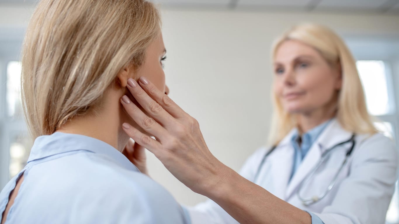 Ärztin tastet die Hals-Ohren-Region einer Patientin ab.