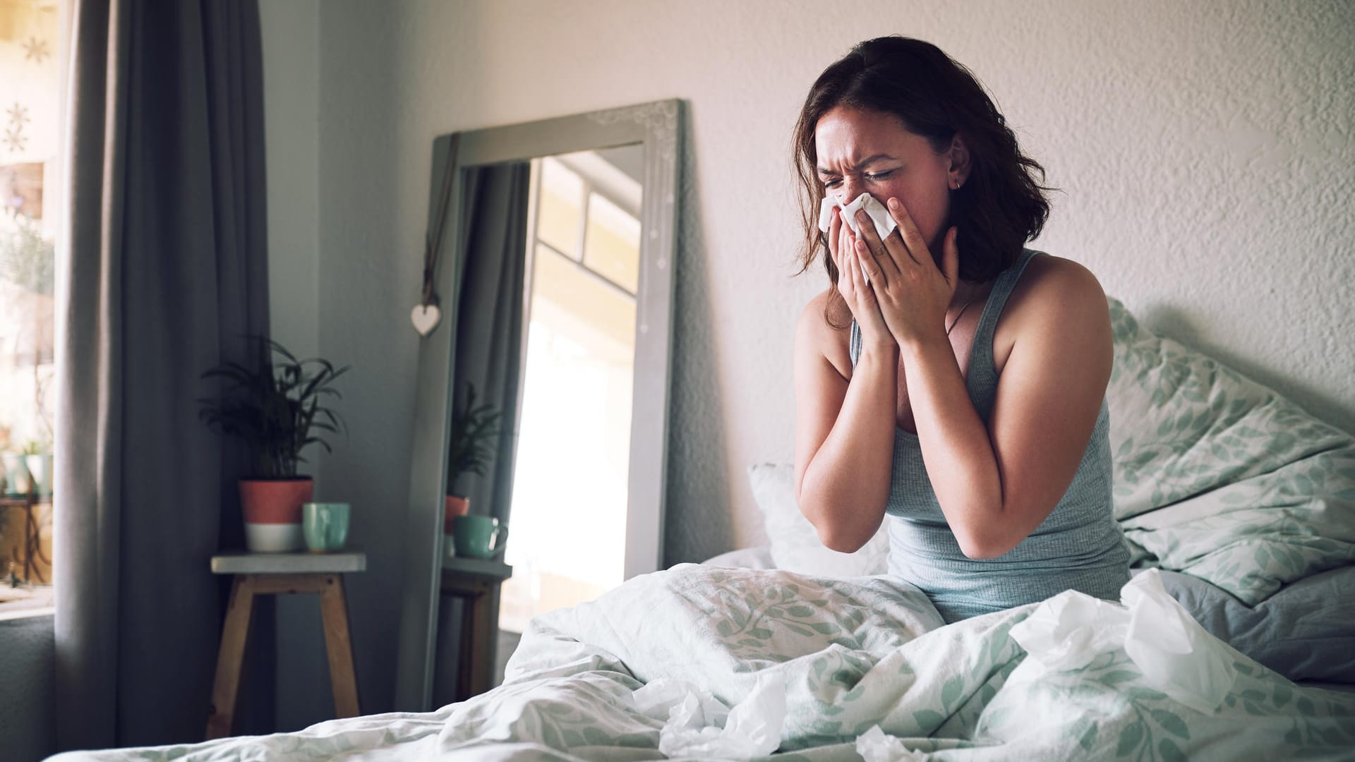 Eine Frau sitzt im Bett und putzt sich die Nase.