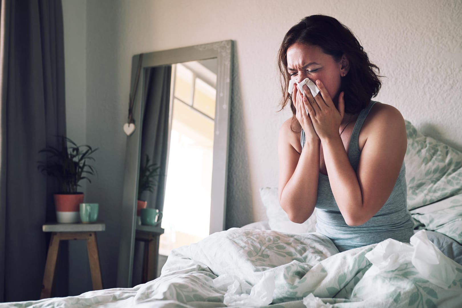 Eine Frau sitzt im Bett und putzt sich die Nase.