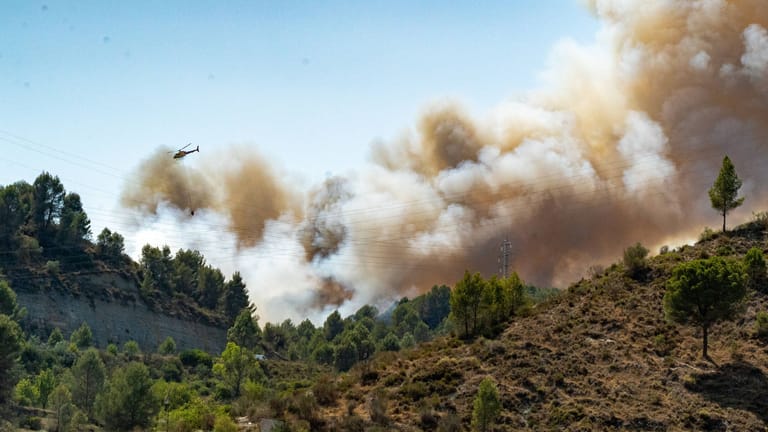 Ein Löschhubschrauber fliegt über ein brennendes Waldstück in Spanien (Archivbild): Nahe der bei Deutschen beliebten Costa Blanca Tausende Hektar in Flammen.