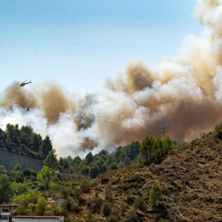Ein Löschhubschrauber fliegt über ein brennendes Waldstück in Spanien (Archivbild): Nahe der bei Deutschen beliebten Costa Blanca Tausende Hektar in Flammen.