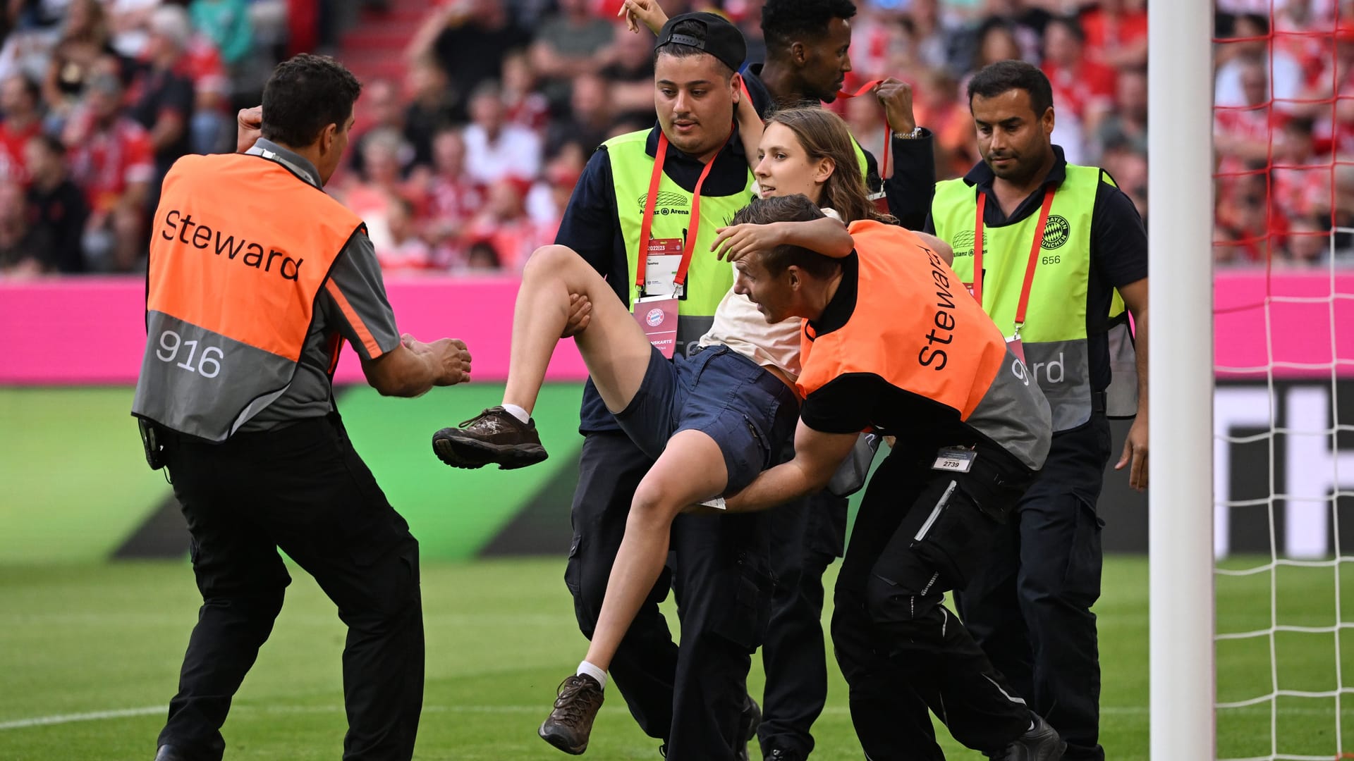 Spiel unterbrochen: Eine Frau wird von Sicherheitskräften vom Spielfeld in der Allianz Arena getragen.