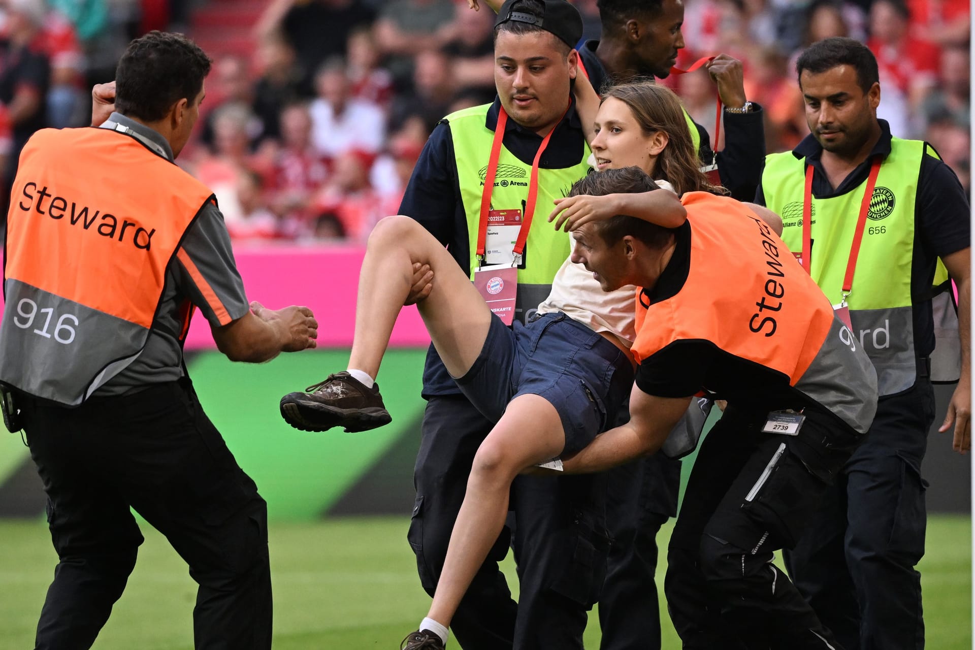 Spiel unterbrochen: Eine Frau wird von Sicherheitskräften vom Spielfeld in der Allianz Arena getragen.
