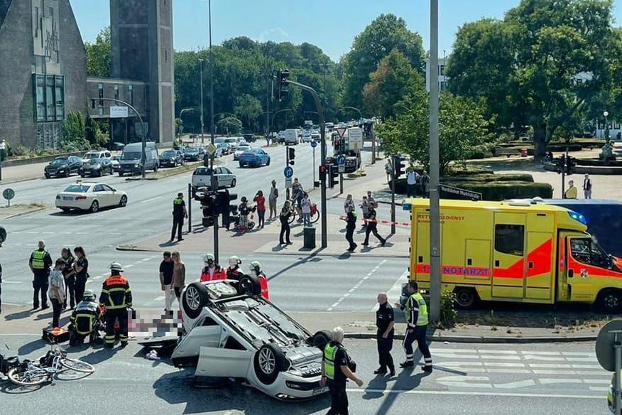 Ein Unfallauto hat sich überschlagen und ist auf dem Dach liegengeblieben. Einsatzkräfte behandeln eine Radfahrerin.