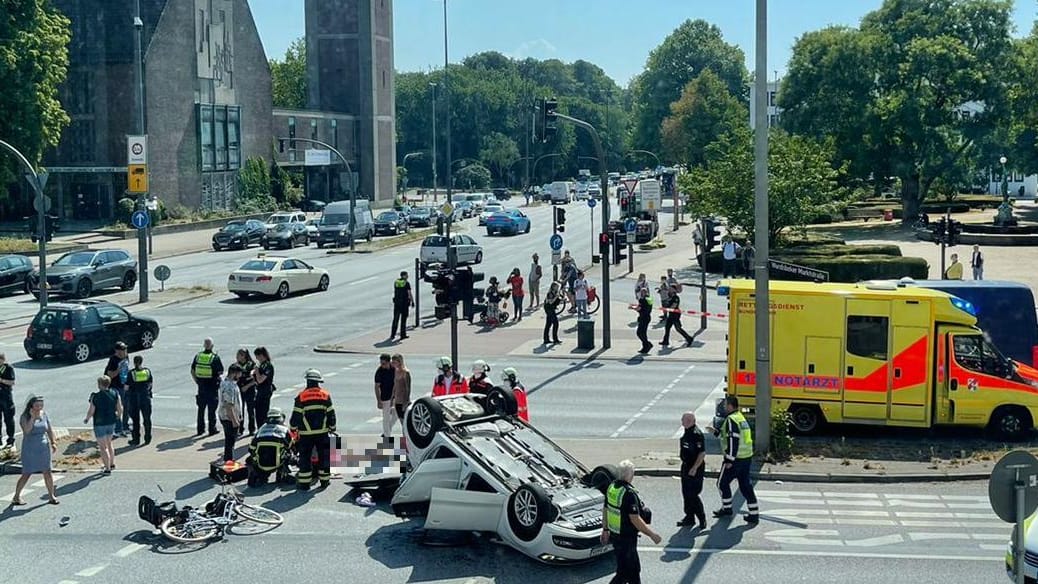 Ein Unfallauto hat sich überschlagen und ist auf dem Dach liegengeblieben. Einsatzkräfte behandeln eine Radfahrerin.