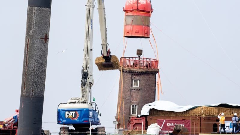 Ein Kran hebt die historische Kuppel von dem schiefen Leuchtturm auf der Mole ab. Ein Kran hebt die historische Kuppel von dem schiefen Leuchtturm auf der Mole ab.