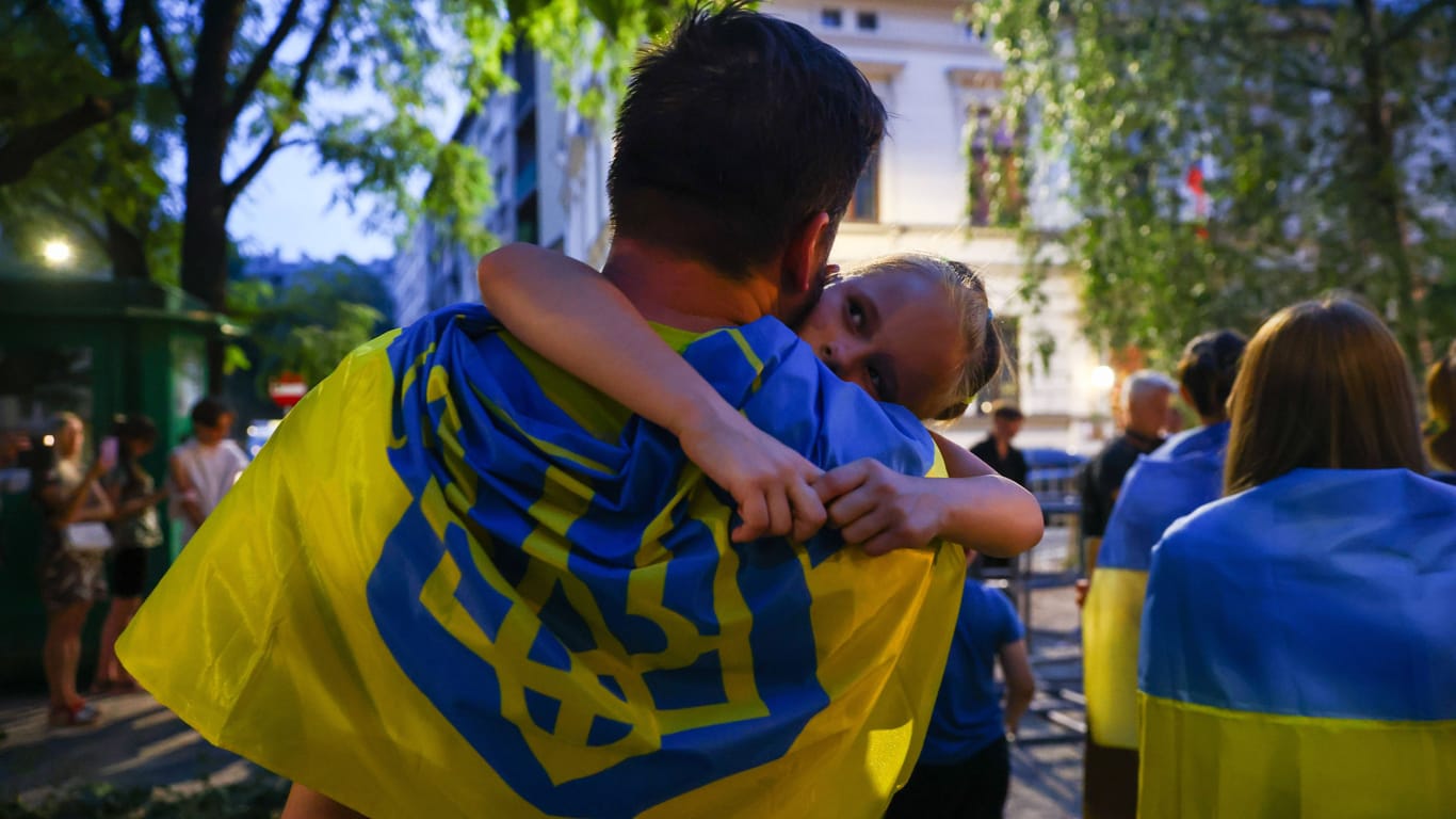 Vater mit Kind und ukrainischer Flagge (Symbolbild): Auch weiterhin erhalten Geflüchtete aus der Ukraine Asyl in Deutschland.