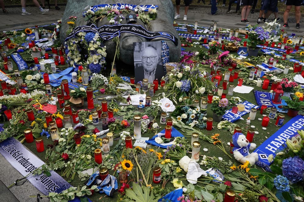 Ein Foto von Uwe Seeler und Blumen, Fan-Schals und Trauerlichter stehen am "Uwe-Seeler-Fuß" vor dem Volksparkstadion: Am Mittwoch findet die Trauerfeier statt.