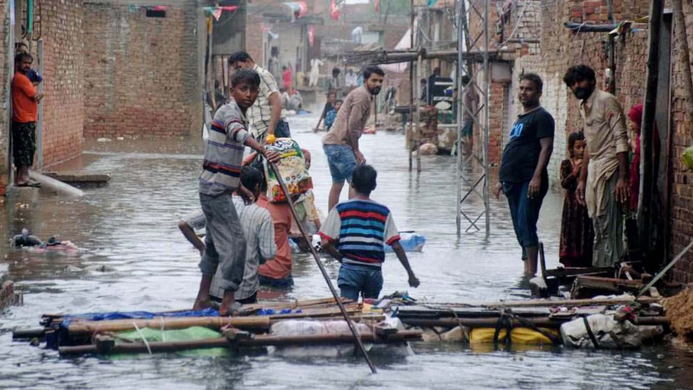 Pakistan, Hyderabad: Menschen waten durch das Hochwasser überschwemmter Straßen nach schweren Monsunregenfällen.