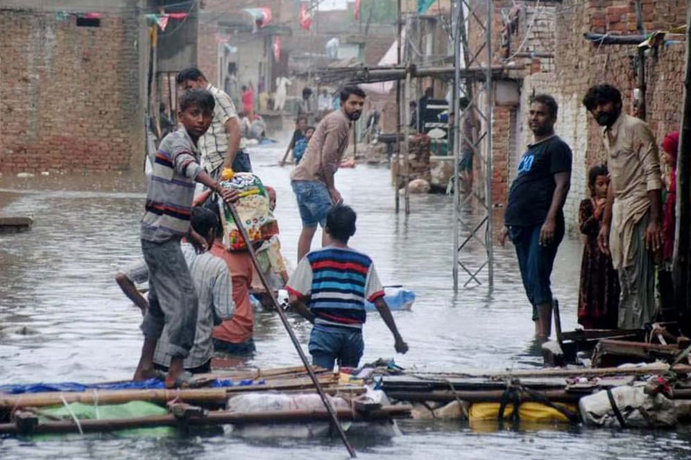 Pakistan, Hyderabad: Menschen waten durch das Hochwasser überschwemmter Straßen nach schweren Monsunregenfällen.