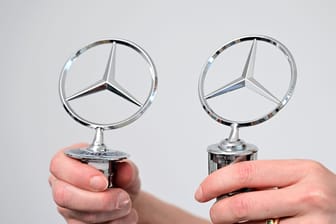 Schwer erkennbare Fälschungen: Ein Original Mercedes-Benz Stern (l) und eine Fälschung (r) werden in einem Büro des Fahrzeugherstellers Mercedes-Benz von zwei Händen gehalten.