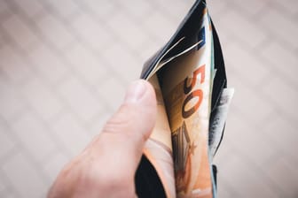 Ein Mann hält einen Geldbeutel mit mehreren Geldscheinen (Symbolbild): Die Deutschen konsumieren aufgrund der andauernden Inflation deutlich weniger.