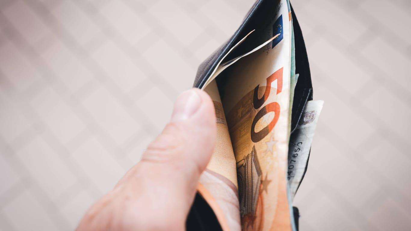 Ein Mann hält einen Geldbeutel mit mehreren Geldscheinen (Symbolbild): Die Deutschen konsumieren aufgrund der andauernden Inflation deutlich weniger.