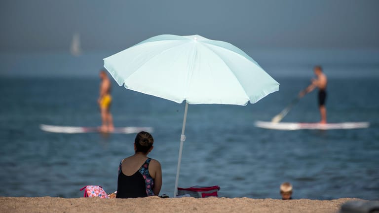 Eine Frau sitzt am Strand unter einem Sonnenschirm (Symbolbild): In den USA kam eine Urlauberin durch einen Schirm ums Leben.