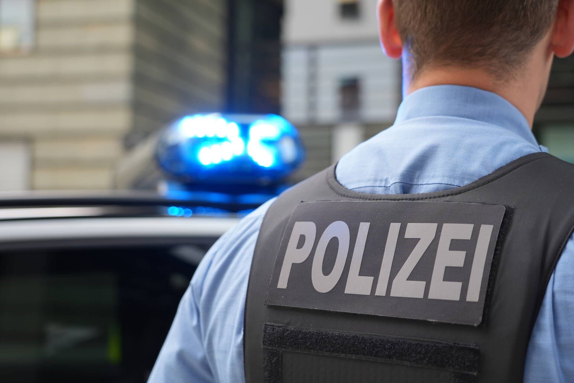 Ein Polizist steht vor einem Einsatzwagen mit Blaulicht (Symbolfoto): Ein 19-Jähriger hatte zu tief ins Glas geschaut.