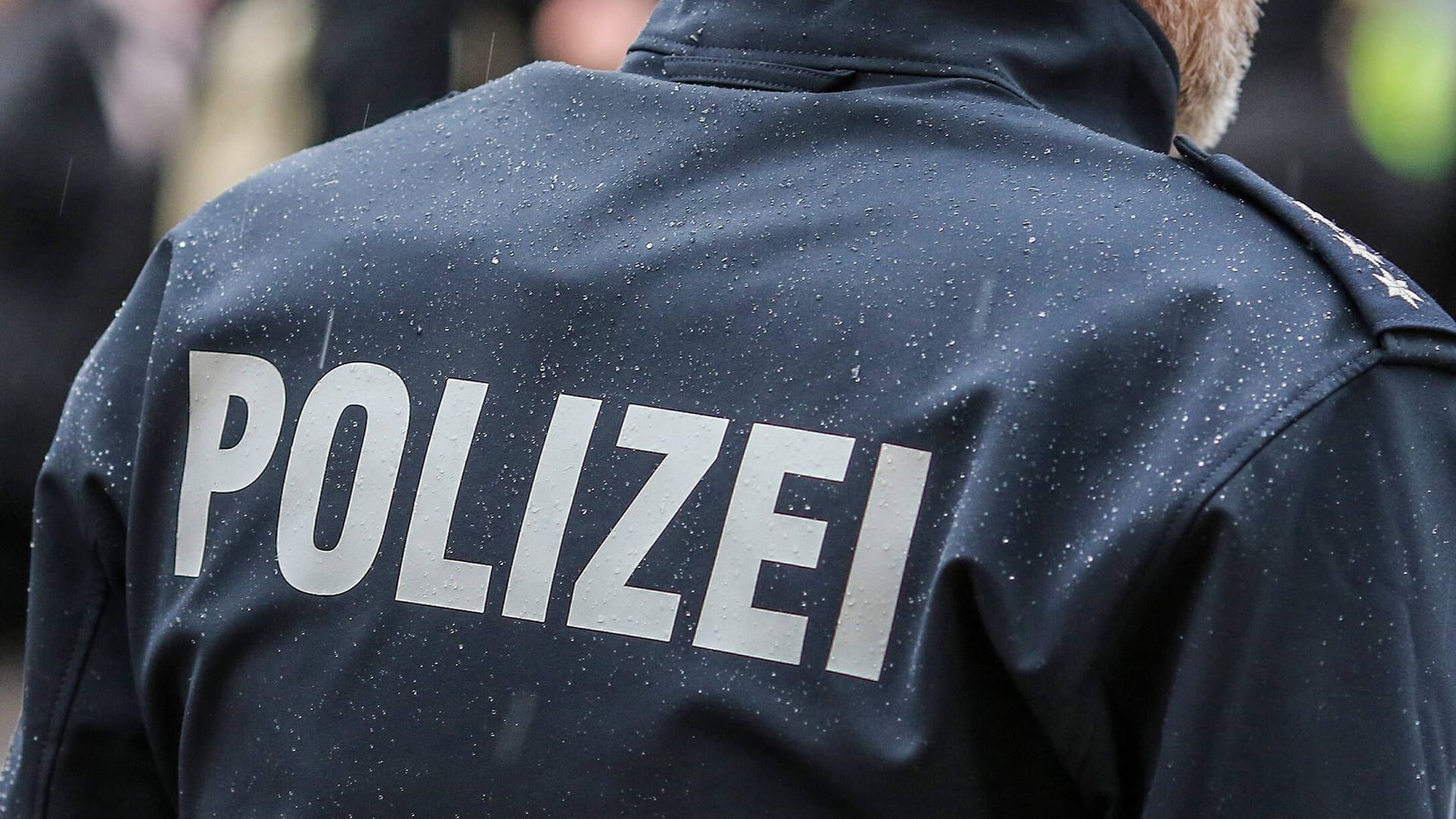 Polizist in Nahaufnahme mit Schutzweste und Schriftzug (Symbolfoto): Die Gruppe floh, die Beamten suchen Zeugen.