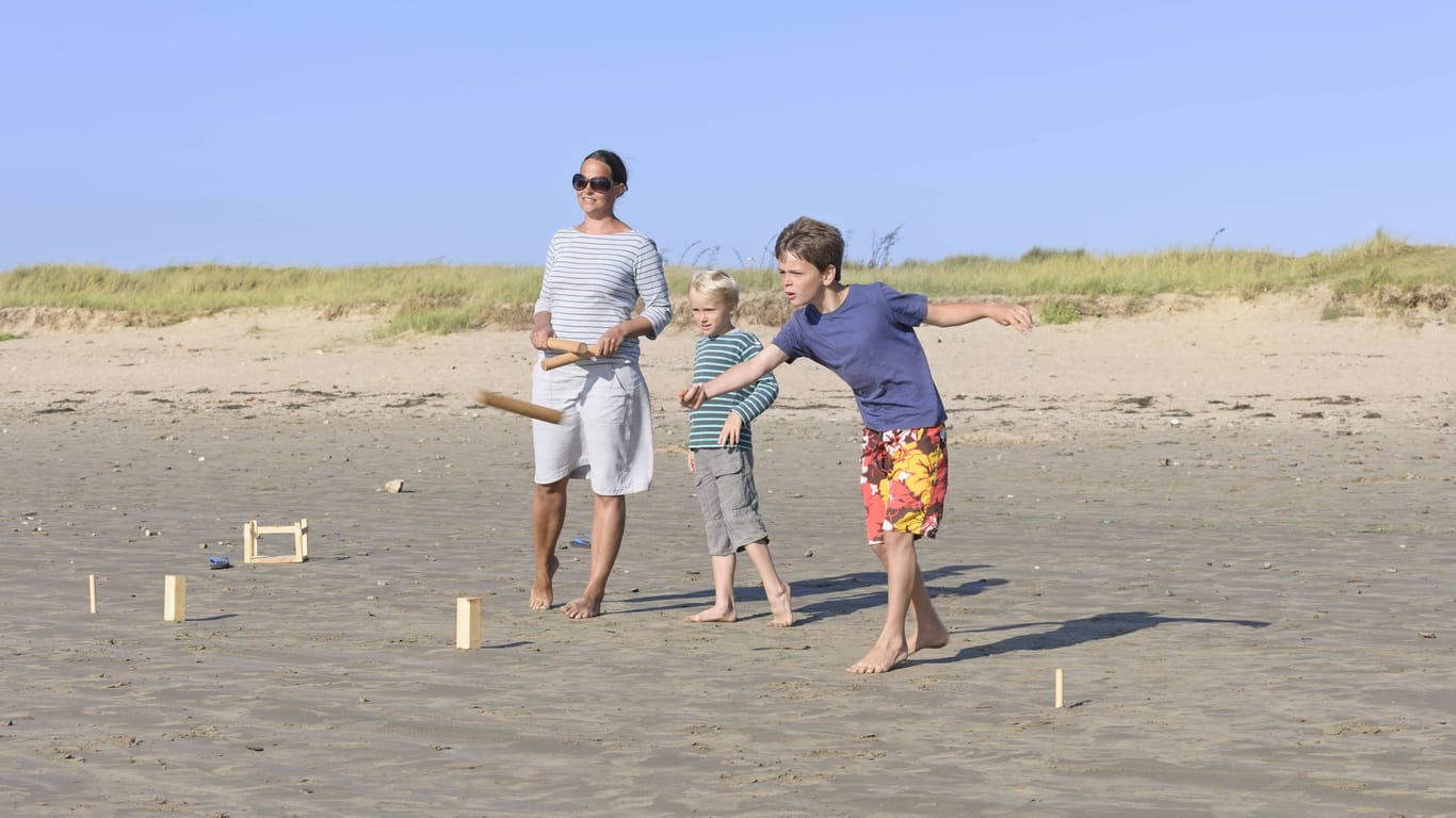 Eine Mutter und ihre zwei Söhne spielen Kubb am Strand.