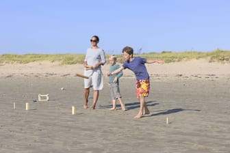 Eine Mutter und ihre zwei Söhne spielen Kubb am Strand.