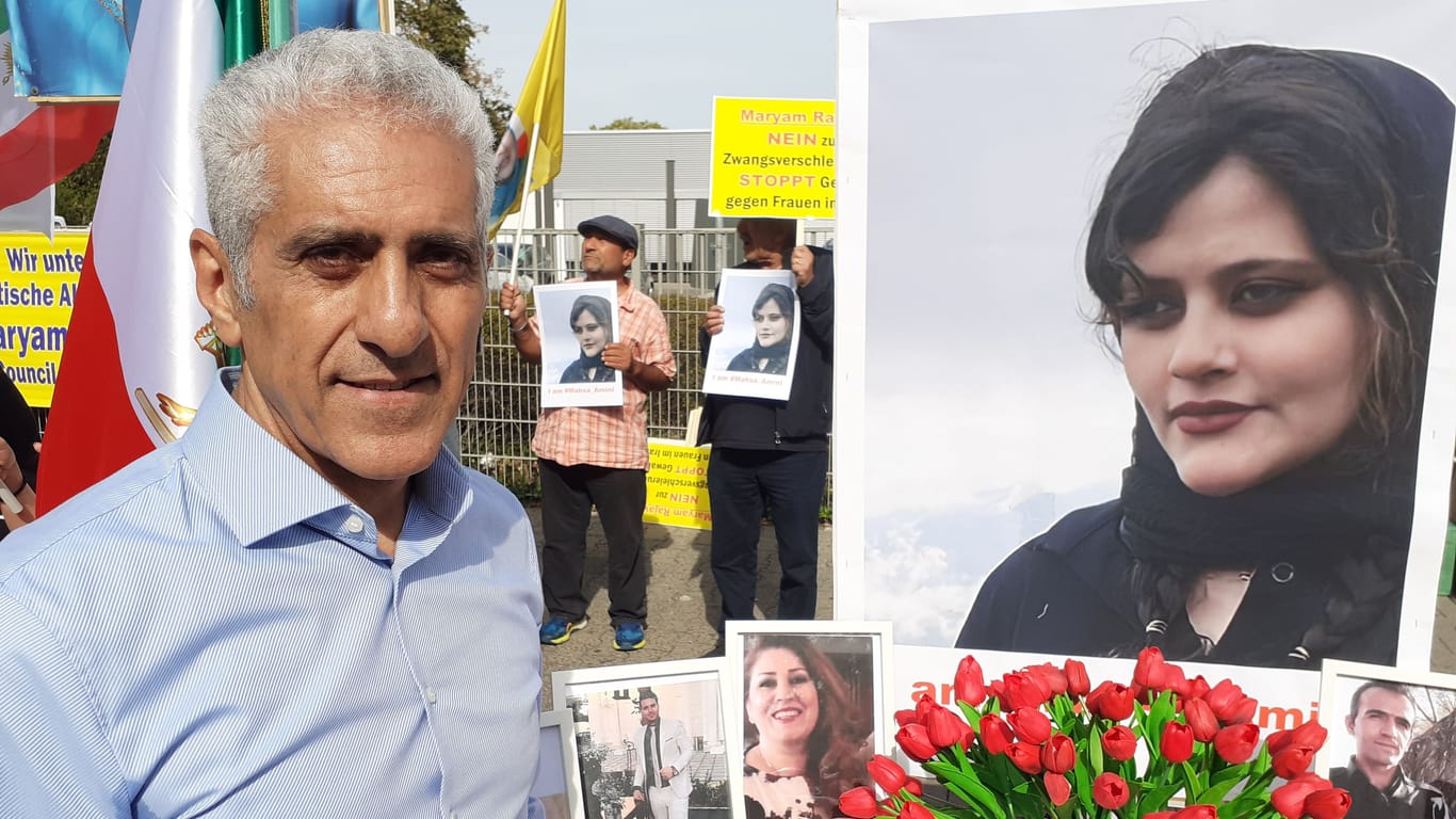 Raza Rouchi lebt seit 1989 in Deutschland: Er steht vor einem Tisch mit Fotos von verstorbenen Protestierenden im Iran.
